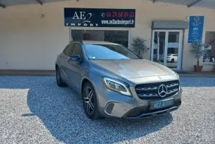 Mercedes GLA gris 3/4 avant droit, avec calandre distinctive et jantes alliage, stationné devant un bâtiment commercial.