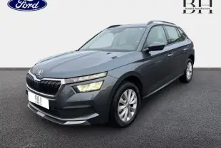 Vue 3/4 avant d'un Skoda Kamiq gris météore avec calandre chromée et phares LED allumés sur fond neutre.
