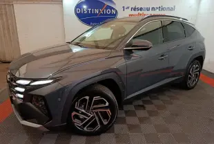 Vue 3/4 avant droit d'un Hyundai Tucson gris foncé 2025 avec jantes alliage et feux LED allumés en intérieur showroom.
