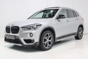 BMW X1 sDrive 18D argent métallisé en 3/4 avant droit avec toit ouvrant et attelage visible.