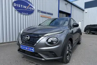 Nissan Juke Hybrid gris squale métal en 3/4 avant droit, avec calandre noire et phares ronds distinctifs.