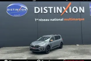 Vue 3/4 avant d'une Dacia Jogger Extreme+ Hybrid 140 2025 gris clair avec jantes noires devant un mur gris.