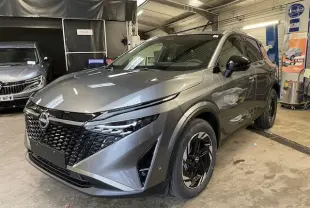 Vue 3/4 avant droit du Nissan Qashqai 2025 gris squale métal avec calandre noire et phares LED fins.