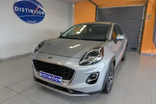 Ford Puma gris en 3/4 avant droit, avec calandre noire et phares LED, stationné en intérieur showroom.