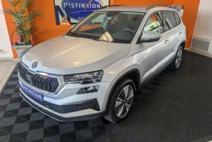 Vue 3/4 avant droite d'un Skoda Karoq gris argent exposé en intérieur avec jantes alliage et calandre chromée.