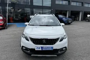 Peugeot 2008 blanc vue de face, avec calandre noire et badge lion, stationnée devant un garage de véhicules d'occasion.