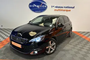 Peugeot 308 noire vue 3/4 avant droit avec phares allumés et jantes alliage dans showroom.