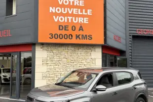 Vue 3/4 avant droite d'un Citroën C3 Aircross électrique gris foncé garé devant un bâtiment commercial.