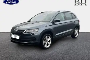 SUV Skoda Karoq gris Business vu en 3/4 avant droit, avec jantes alliage et barres de toit visibles.