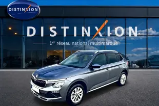SKODA KAMIQ gris en 3/4 avant droit, avec calandre chromée et barres de toit blanches visibles.