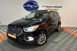 Ford Kuga noir en 3/4 avant droit, avec calandre hexagonale et feux LED allumés dans un showroom.