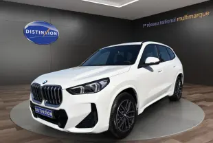 BMW X1 sDrive20d blanc vue 3/4 avant droit en showroom avec calandre noire et jantes foncées.
