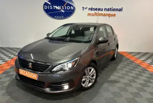 Peugeot 308 gris vue 3/4 avant droit dans showroom avec plaque orange "OCCASION" et logo Distinxion au mur.