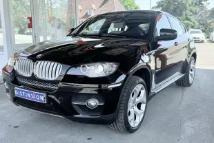 BMW X6 noire vue de 3/4 avant droit, avec calandre chromée et jantes argentées visibles sous abri.