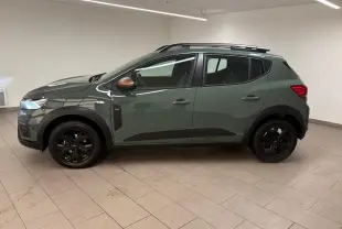 Vue de profil côté gauche d'une Dacia Sandero Stepway 2023 vert cèdre avec jantes noires et barres de toit.