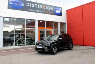 Dacia Duster III noir nacré vu en 3/4 avant droit devant un bâtiment commercial Distinxion.