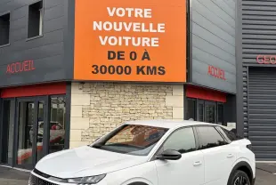 Peugeot 3008 blanc en 3/4 avant droit, avec jantes noires et calandre distinctive, devant un bâtiment commercial.