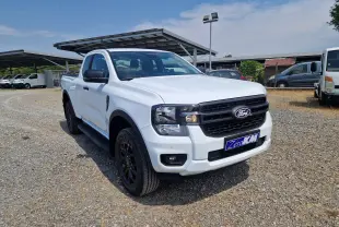 Ford Ranger Super Cabine blanc vu en 3/4 avant droit, avec calandre noire et roues noires sur terrain gravillonné.