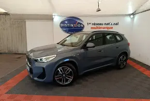 BMW X1 xDrive25e M Sport gris foncé vue 3/4 avant droit en intérieur sur sol noir et rouge.