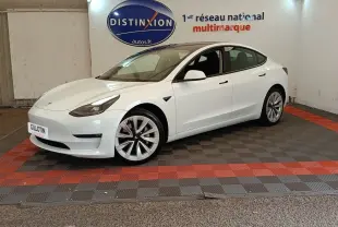 Tesla Model 3 Grande Autonomie blanc vue 3/4 avant droit, stationnée sur sol à damiers rouge et noir en intérieur.