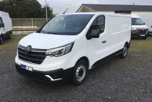 Renault Trafic Fourgon blanc en 3/4 avant droit, avec calandre noire et feux LED, stationné sur sol gravillonné.