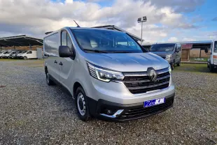 Vue 3/4 avant droit d'un Renault Trafic Fourgon gris Highland avec calandre noire et feux LED allumés sur un parking.