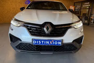 Vue avant d'un Renault Arkana blanc nacré avec calandre noire et phares LED allumés en intérieur showroom.