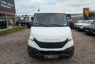 Vue frontale d'un utilitaire Iveco Daily blanc avec calandre noire et phares allumés sur un parking.