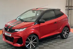Vue 3/4 avant droite d'une Aixam Ambition rouge 2026 avec bandes noires sur capot et jantes alliage noires.