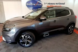 Vue de profil droit du Citroën C5 Aircross gris foncé avec jantes alliage et barres de toit chromées en intérieur showroom.