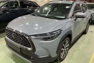 Toyota Corolla Cross gris Manhattan vue 3/4 avant droit, mettant en valeur sa calandre imposante et ses phares LED fins.