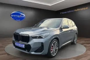 BMW X1 Storm Bay en 3/4 avant droit, jantes alliage 20'' et freins M Sport rouges visibles dans un showroom.