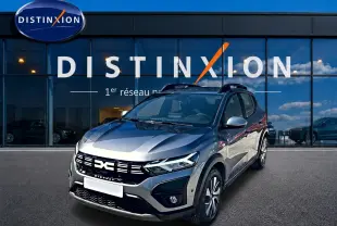 Dacia Sandero Stepway gris schiste vue 3/4 avant droit avec barres de toit devant un bâtiment Distinxion.