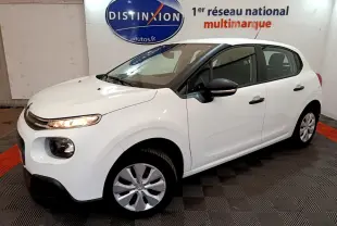 Citroën C3 blanche vue en 3/4 avant droit, avec feux allumés et rétroviseurs noirs dans un showroom.