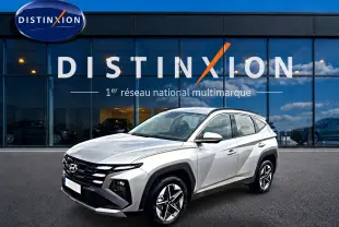Hyundai Tucson gris shimmering en 3/4 avant droit devant une vitrine Distinxion, jantes alu et lignes anguleuses visibles.