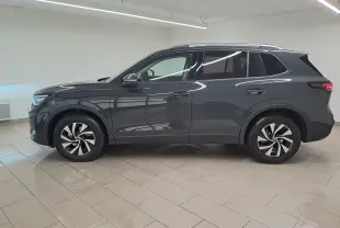 Vue de profil côté gauche du Volkswagen Tiguan 2024 gris Urano avec jantes distinctives et attelage escamotable visible.