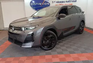 Vue 3/4 avant d'une Citroën C5 hybride gris foncé avec jantes noires et calandre moderne, en intérieur showroom.