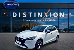 Vue 3/4 avant droite d'une Mazda2 blanche 2024 avec calandre noire et jantes distinctives devant un showroom Distinxion.