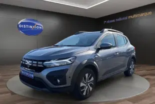 Vue 3/4 avant d'une Dacia Sandero Stepway gris foncé avec barres de toit et jantes alliage en showroom.