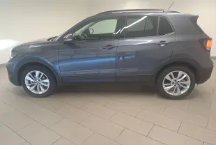 Vue de profil côté gauche d'un Volkswagen T-Cross 2025 gris cendré métallisé avec jantes alliage et feux arrière allumés.