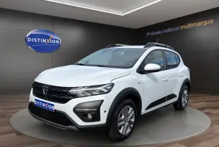 Dacia Sandero Stepway blanc vue 3/4 avant droit, avec barres de toit et protections noires sur les bas de caisse.
