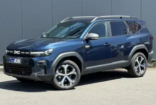 SUV Dacia Bigster bleu indigo en 3/4 avant droit avec barres de toit et jantes alliage diamantées.