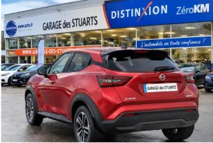 Vue 3/4 arrière droite du Nissan Juke rouge Fuji Sunset garé devant un garage avec jantes alliage 17 pouces.