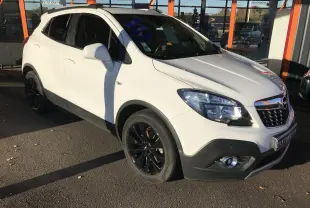 Opel Mokka blanc vue 3/4 avant droit, jantes noires et calandre chromée, stationné devant un bâtiment vitré.