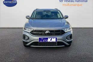 Vue frontale d'un Volkswagen T-Roc gris pyrite métal 2025 avec calandre noire et phares LED allumés.