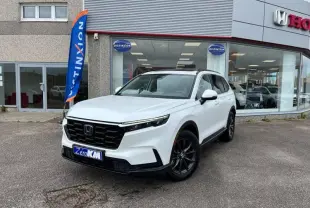 Honda CR-V blanc platine nacré vu en 3/4 avant droit devant un concessionnaire avec toit noir et jantes foncées.