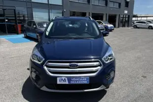 Vue frontale d'un Ford Kuga bleu foncé 2018 avec calandre chromée, stationné devant un bâtiment commercial.