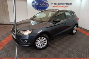 SEAT Arona gris clair en 3/4 avant droit, avec jantes alliage et feux allumés dans un showroom intérieur.