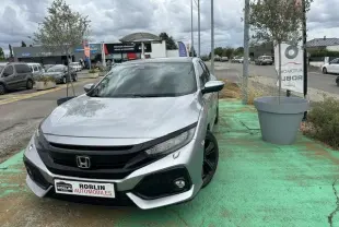 Vue 3/4 avant d'une Honda Civic grise stationnée, avec jantes noires et calandre noire distinctive.