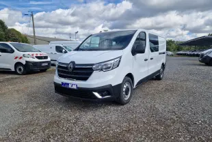 Renault Trafic cabine approfondie blanc en 3/4 avant droit sur parking gravillonné, avec calandre noire et phares modernes.